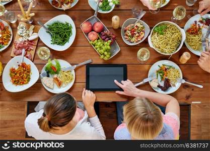 eating, people and technology concept - women with tablet pc computer sitting at table full of food. women with tablet pc at table full of food