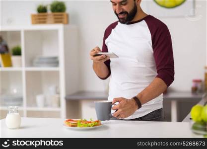 eating, people, technology and diet concept - man with smartphone having vegetable sandwiches and coffee for breakfast at home kitchen. man with smartphone and coffee eating at home