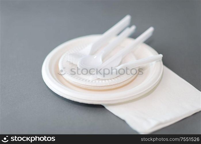 eating, recycling and ecology concept - disposable paper plates and plastic spoons, knives and forks on grey background. paper plates and plastic spoons, knives and forks