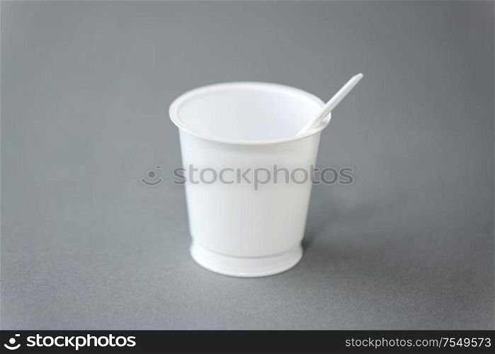 eating, recycling and ecology concept - white disposable plastic cup with spoon on grey background. white disposable plastic cup with spoon