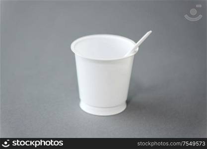eating, recycling and ecology concept - white disposable plastic cup with spoon on grey background. white disposable plastic cup with spoon