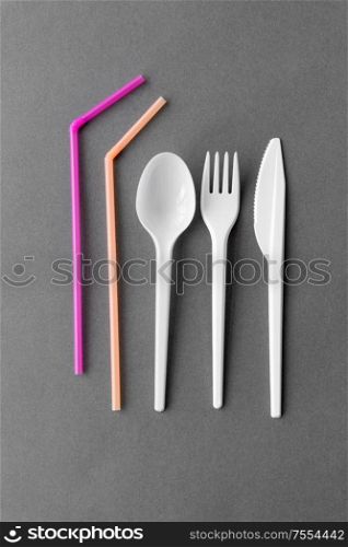 eating, recycling and ecology concept - white disposable plastic fork, knife and spoon with pink straws on grey background. disposable plastic fork, knife, spoon and straws
