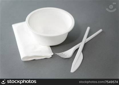 eating, recycling and ecology concept - white disposable plastic plate with fork, knife and paper napkin on grey background. disposable plastic plate with fork and knife
