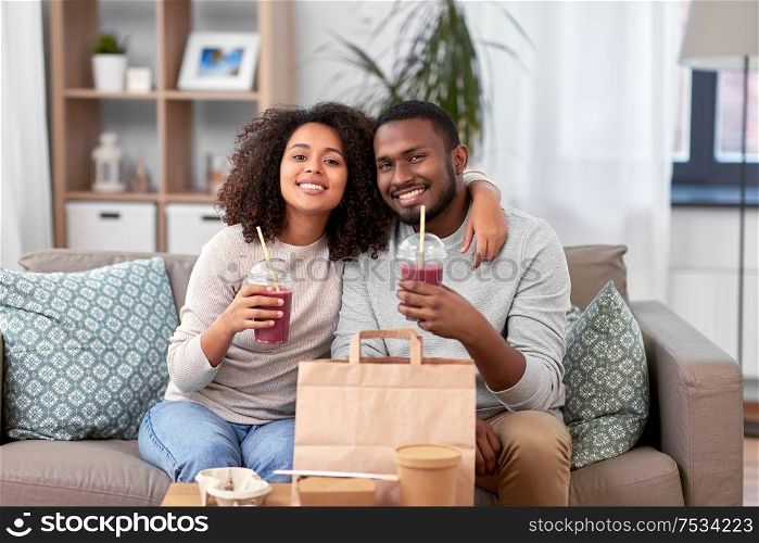 eating, relations and people concept - happy african american couple with takeaway food and drinks at home. happy couple with takeaway food and drinks at home