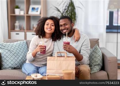 eating, relations and people concept - happy african american couple with takeaway food and drinks at home. happy couple with takeaway food and drinks at home