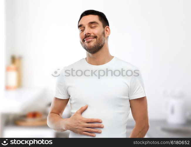 eating, satisfaction and people concept - happy full man touching his tummy over kitchen background