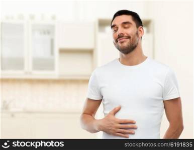 eating, satisfaction and people concept - happy full man touching his tummy over kitchen background