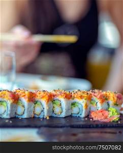 Eating sushi in the restaurant, a woman using chopsticks takes a piece of a roll, enjoying tasty and healthy food, traditional Asian dish
