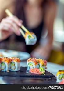 Eating sushi in the restaurant, a woman using chopsticks takes a piece of roll, enjoying tasty and healthy food, traditional Asian cuisine