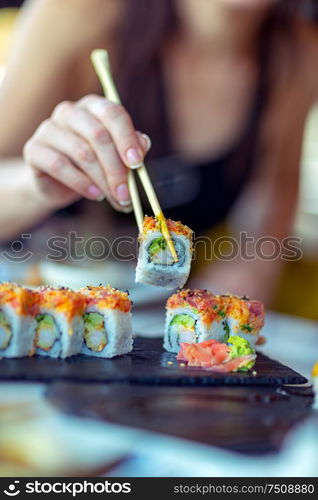 Eating sushi in the restaurant, a woman with a perfect manicure using chopsticks takes a piece of roll, enjoying tasty and healthy food, traditional Asian dish