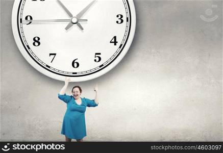 Eating systematic. Middle aged stout woman in blue dress pointing at clock