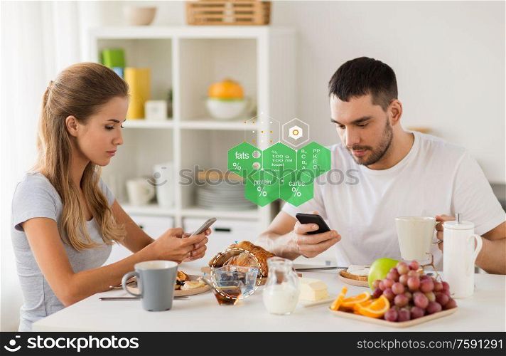 eating, technology and people concept - couple with smartphones having breakfast at home over food nutritional value chart. couple with smartphones having breakfast at home