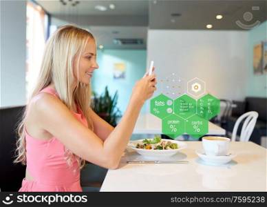 eating, technology and people concept - happy woman with smartphone and salad for lunch at restaurant over food nutritional value chart. happy woman with smartphone eating at restaurant