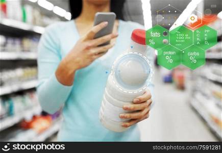 eating, technology and people concept - young woman with smartphone holding milk bottle at grocery store or supermarket over food nutritional value chart. woman with smartphone buying milk at supermarket