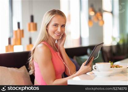 eating, technology, people and leisure concept - happy young woman with tablet pc computer and food listening to music at restaurant. happy young woman with tablet pc at restaurant