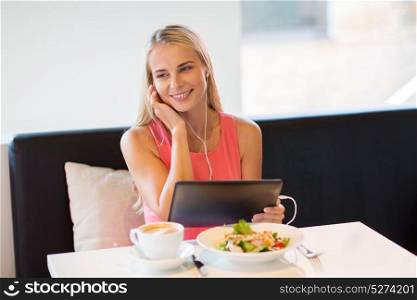 eating, technology, people and leisure concept - happy young woman with tablet pc computer and food listening to music at restaurant. happy young woman with tablet pc at restaurant