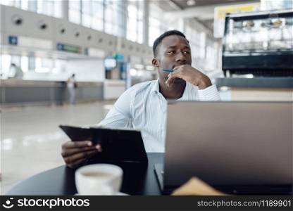 Ebony businessman sitting at laptop in car dealership. Successful business person on motor show, black man in formal wear, automobile showroom