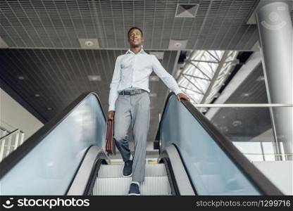 Ebony businessman with briefcase descending on the escalator in mall. Successful business person, black man in formal wear, shopping center