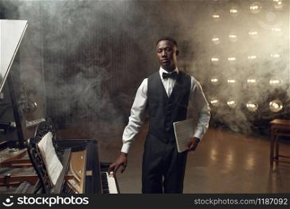 Ebony grand piano player playing on the stage with spotlights on background. Negro performer poses at musical instrument before concert. Ebony grand piano player playing on the stage