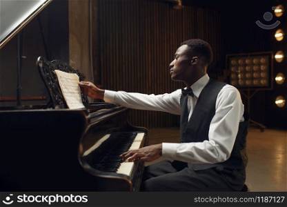 Ebony pianist, jazz performer on the stage with spotlights on background. Negro musician poses at musical instrument before concert. Ebony pianist, jazz performer on the stage