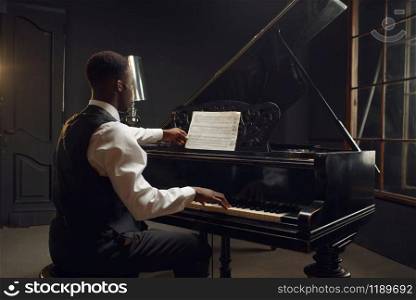 Ebony pianist, jazz performer on the stage with spotlights on background. Negro musician poses at musical instrument before concert. Ebony pianist, jazz performer on the stage