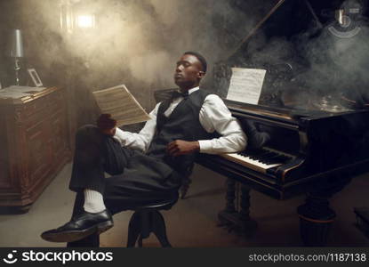 Ebony pianist with music notebook, jazz musician. Negro performer poses at musical instrument before concert. Ebony pianist with music notebook, jazz musician
