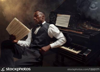 Ebony pianist with music notebook, jazz musician. Negro performer poses at musical instrument before concert