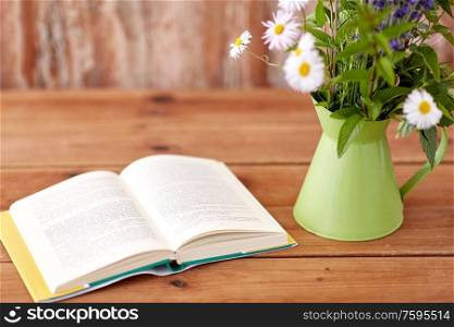 eco and organic concept - book and flowers in jug on wooden table. book and flowers in jug on wooden table