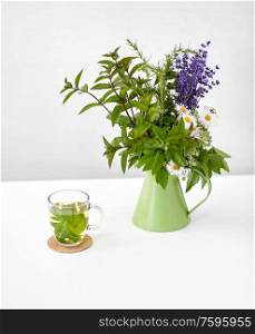 eco and organic concept - herbal tea and flowers in green jug on on white background. herbal tea and flowers in jug