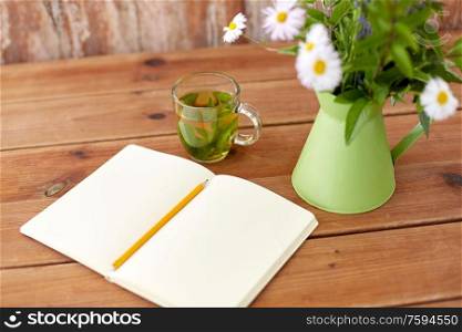 eco and organic concept - herbal tea, notebook with pencil and flowers in green jug on table. herbal tea, notebook and flowers in jug on table