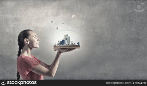 Eco city concept. Young woman in red dress holding opened book with city model