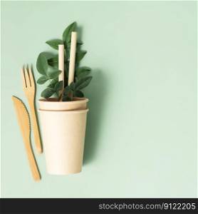Eco composition with tableware on light green background. Eco natural paper cups, bamboo cutlery and green leaves flat lay copy space square