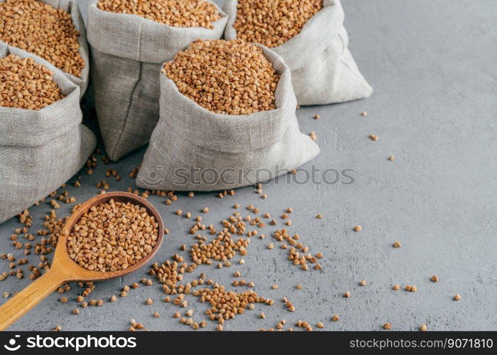 Eco food and clean eating concept. Buckwheat in small linen bags. Wooden spoon filled with protein product, Copy space on grey background.