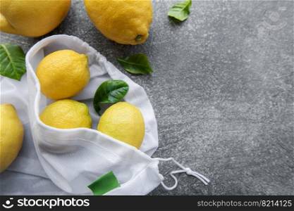 Eco-friendly bag with ripe lemons on concrete background