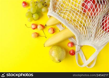 Eco-friendly cotton shopping bag. Ripe fruits in a mesh bag on a yellow background. Organic vegan food. Sustainable lifestyle and zero waste concept.. Eco-friendly cotton shopping bag. Ripe fruits in mesh bag on yellow background. Organic vegan food. Sustainable lifestyle and zero waste concept.