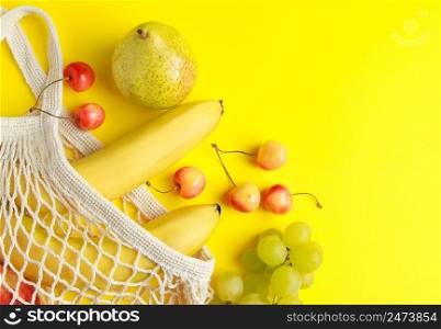 Eco-friendly cotton shopping bag. Ripe fruits in a mesh bag on a yellow background. Organic vegan food. Sustainable lifestyle and zero waste concept.. Eco-friendly cotton shopping bag. Ripe fruits in mesh bag on yellow background. Organic vegan food. Sustainable lifestyle and zero waste concept.