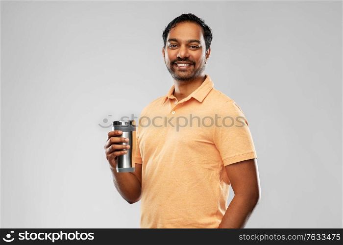 eco living and sustainability concept - happy smiling young indian man in polo t-shirt with thermo cup or tumbler for hot drinks over grey background. indian man with thermo cup or tumbler for drink