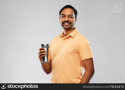 eco living and sustainability concept - happy smiling young indian man in polo t-shirt with thermo cup or tumbler for hot drinks over grey background. indian man with thermo cup or tumbler for drink