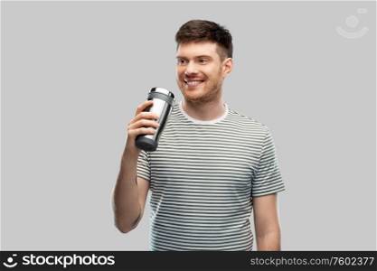 eco living and sustainability concept - happy smiling young man in striped t-shirt with thermo cup or tumbler for hot drinks over grey background. man with thermo cup or tumbler for hot drinks