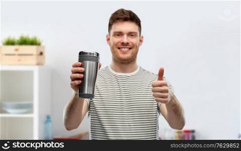 eco living and sustainability concept - happy smiling young man in striped t-shirt with thermo cup or tumbler for hot drinks over home kitchen background. man with thermo cup or tumbler for hot drinks