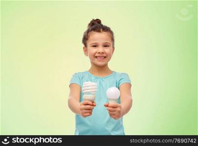 eco living and sustainability concept - smiling girl comparing energy saving light bulb with incandescent lamp over green background. smiling girl comparing different light bulbs