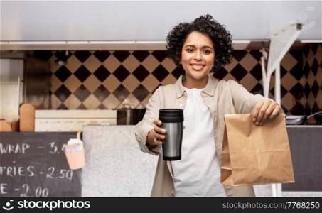 eco living, eating and sustainability people concept - happy smiling woman with thermo cup and takeaway paper bag over food truck background. happy woman with thermo cup and food in paper bag
