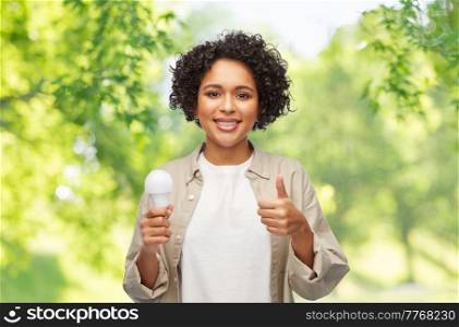 eco living, energy saving and sustainability concept - portrait of happy smiling woman holding lighting bulb over green natural background. happy smiling woman holding lighting bulb