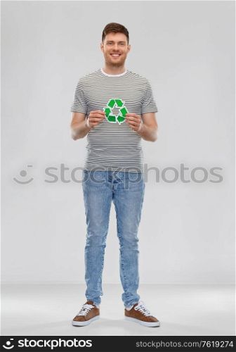 eco living, environment and sustainability concept - happy smiling young man in striped t-shirt holding green recycling sign over grey background. smiling young man holding green recycling sign