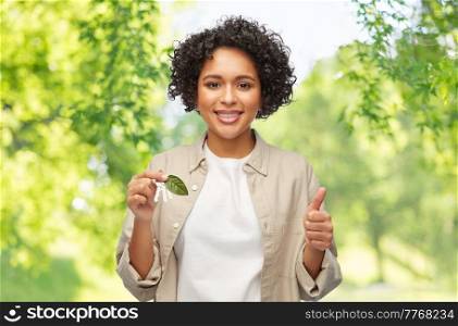 eco living, environment and sustainability concept - portrait of happy smiling woman holding house keys with green leaf over natural background. woman holding house keys with green leaf
