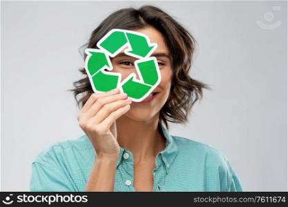 eco living, environment and sustainability concept - portrait of happy smiling young woman in turquoise shirt looking through green recycling sign over grey background. smiling woman looking through green recycling sign
