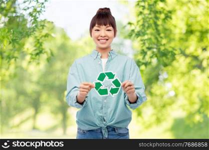 eco living, environment and sustainability concept - portrait of happy smiling young asian woman in turquoise shirt holding green recycling sign over natural background. smiling asian woman holding green recycling sign