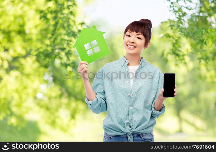 eco living, environment and sustainability concept - portrait of happy smiling young asian woman in turquoise shirt holding green house over natural background. smiling asian woman holding green house