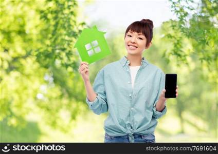 eco living, environment and sustainability concept - portrait of happy smiling young asian woman in turquoise shirt holding green house over natural background. smiling asian woman holding green house