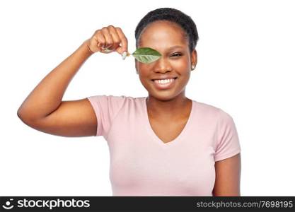 eco living, environment and sustainability concept - portrait of happy smiling young african american woman covering one eye with green leaf over white background. smiling african american woman holding green leaf